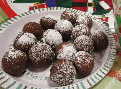 May include: A plate of chocolate-covered balls dusted with powdered sugar. The balls are arranged in a circle on a white plate with green and white stripes.